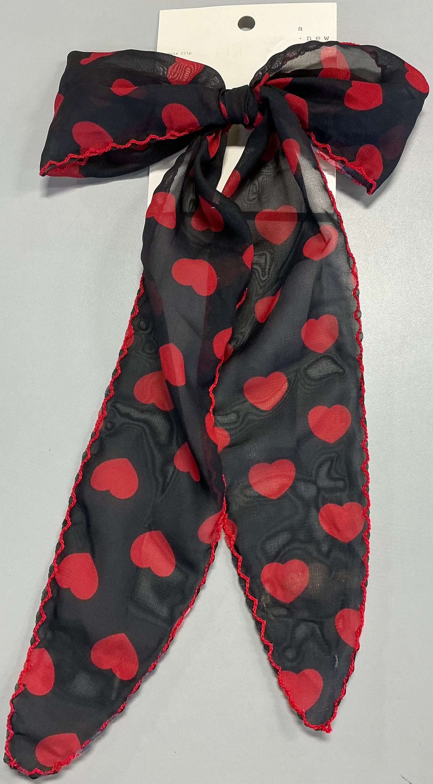 Hair bow featuring a red heart print and red stitching along the edges