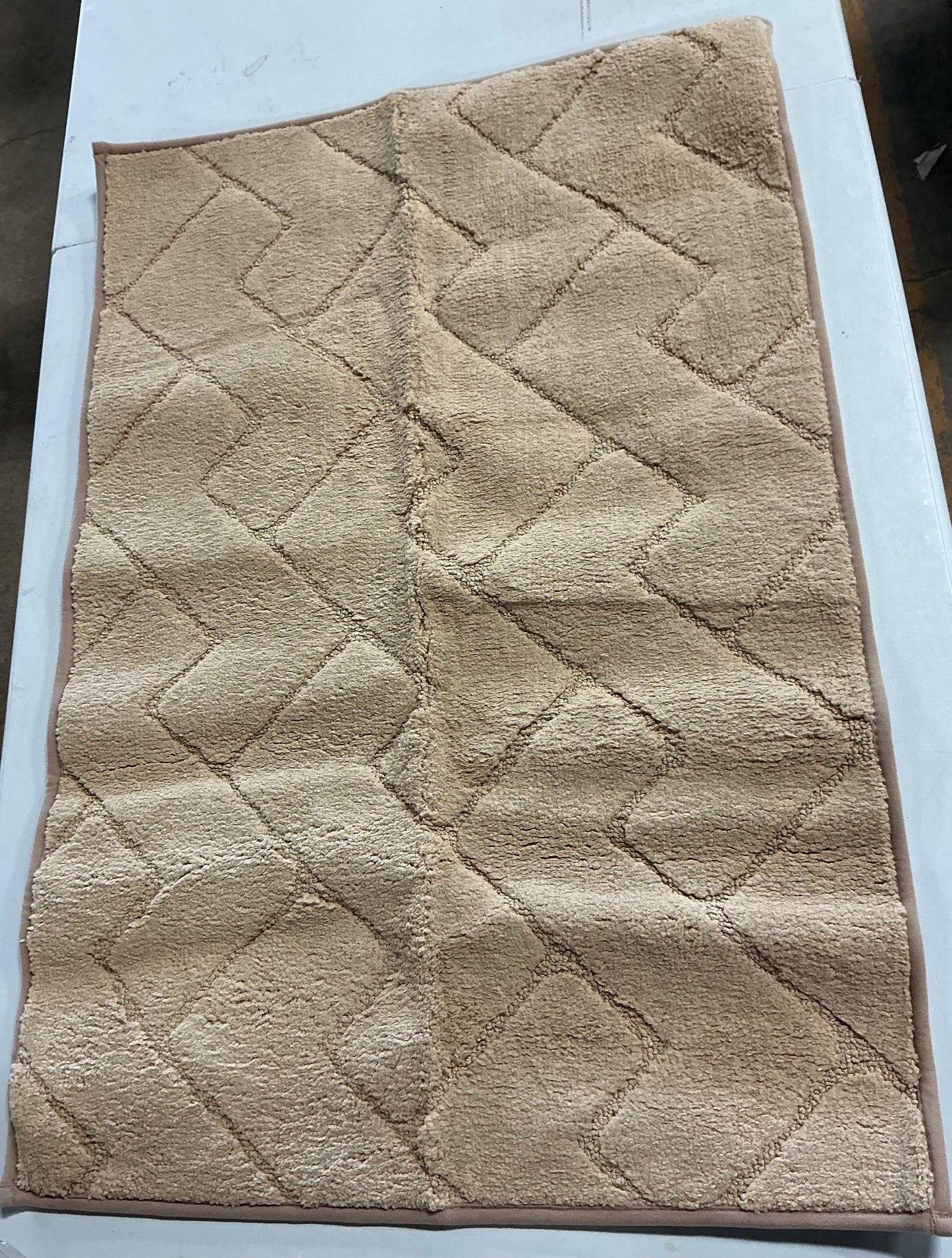 Beige bath mat features a textured, geometric zig-zag pattern and matching piped edges 24 inches x 36 in